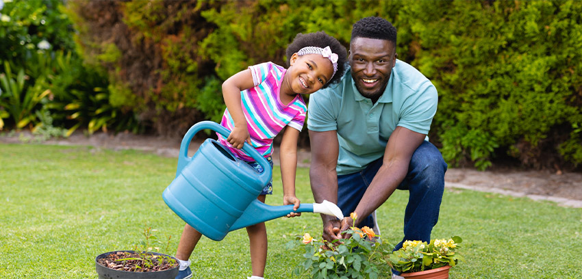Child and adult watering potted plants together in a backyard garden - https://www.sartori-insurance.com/